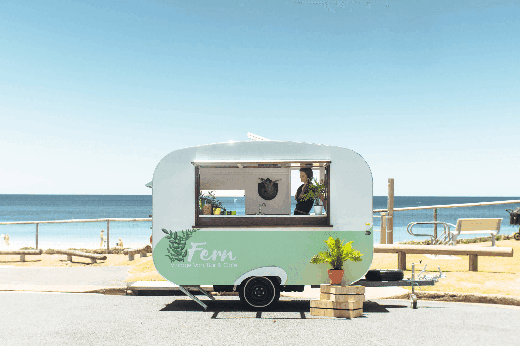 Female bartender of the Fern Vintage Van's mobile bar catering an event located near a beach.