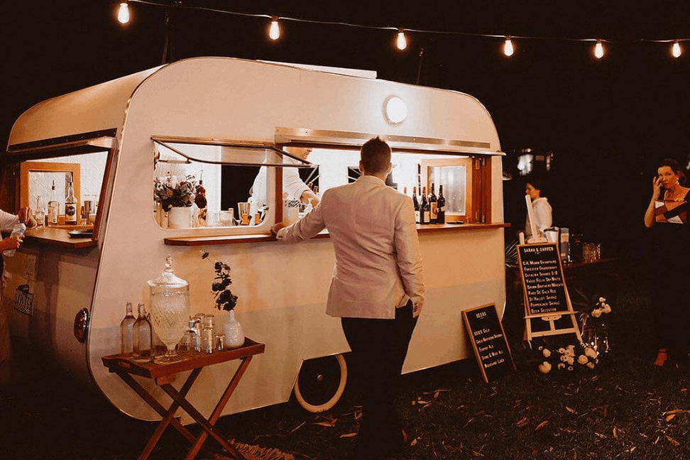 A man standing in front of the mobile bar waiting for the bartender to serve his drink.