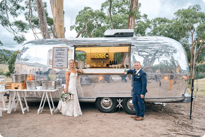 Bride and groom leaning on mobile bar at wedding event